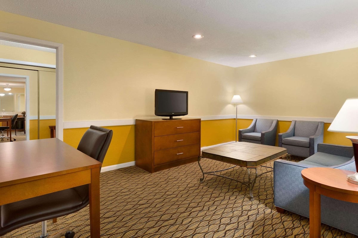 A hotel room with a wooden desk, a television, a sofa, a small table, and a lamp.