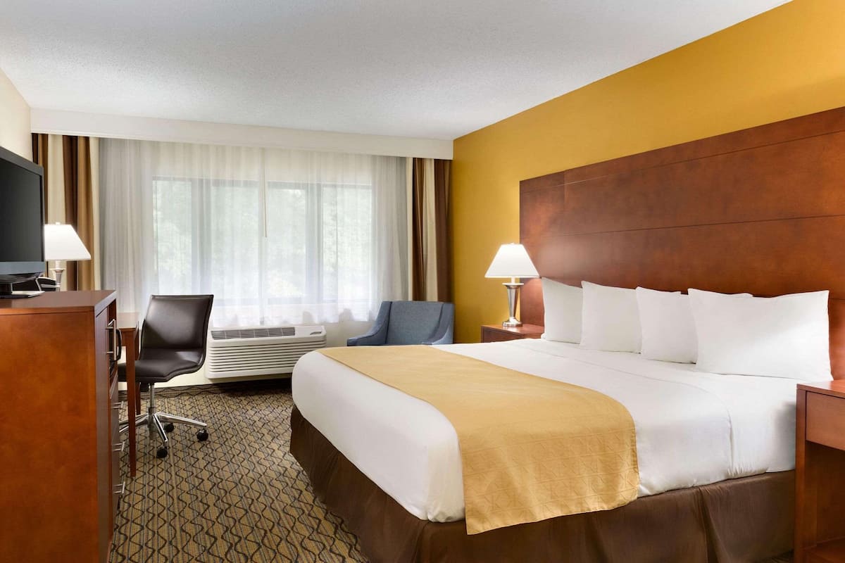 A hotel room with a large bed, a desk with a computer, an air conditioning unit, and a television.
