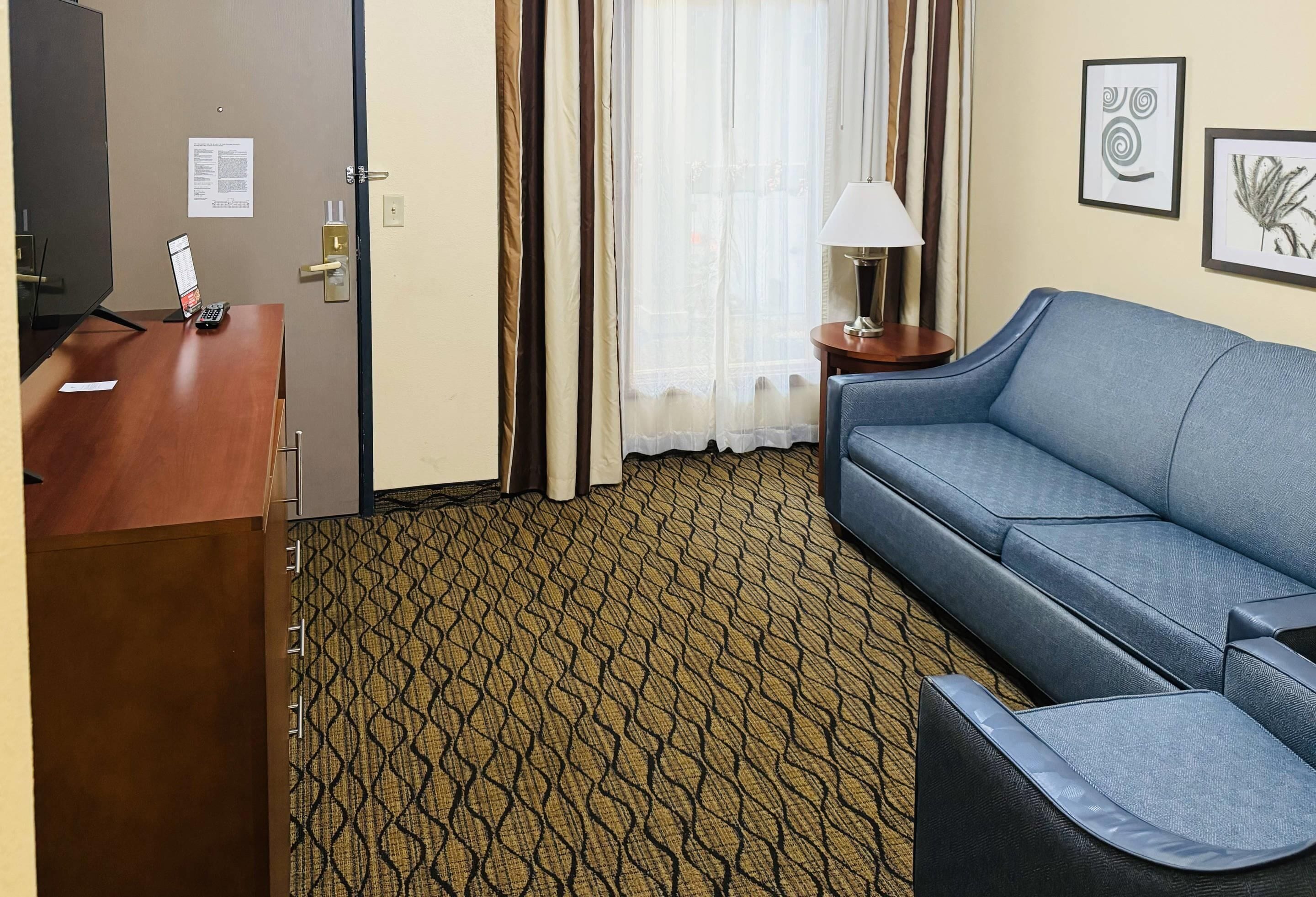 A hotel room with a desk, a blue sofa, a patterned carpet, and a window with curtains.
