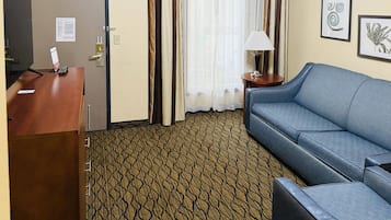 A hotel room with a desk, a blue sofa, a patterned carpet, and a window with curtains.