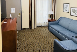 A hotel room with a desk, a blue sofa, a patterned carpet, and a window with curtains. - Country Inn & Suites by Radisson, Mishawaka - South Bend (Mishawaka)