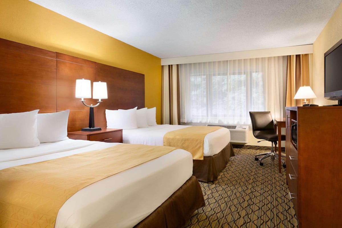 A hotel room with two beds, a desk with a computer, a TV, and a window with curtains.