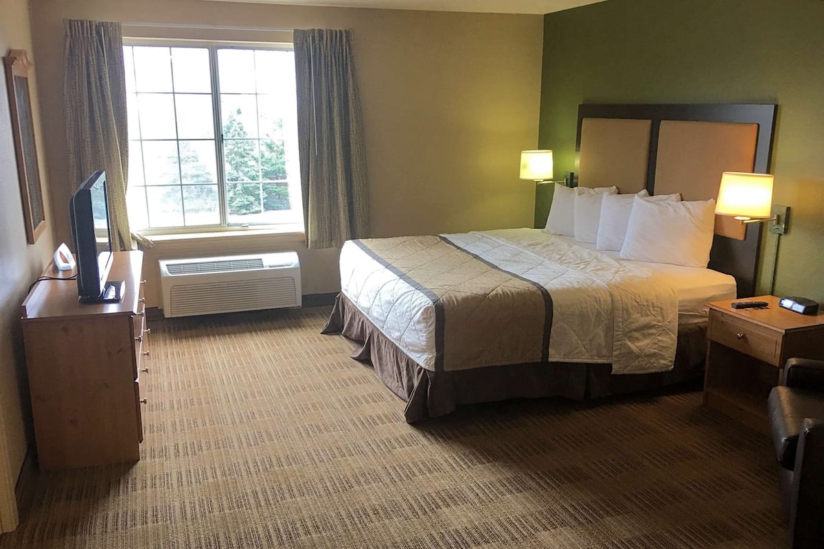 A hotel room with a large bed, two bedside lamps, a TV on a stand, and a window with curtains.
