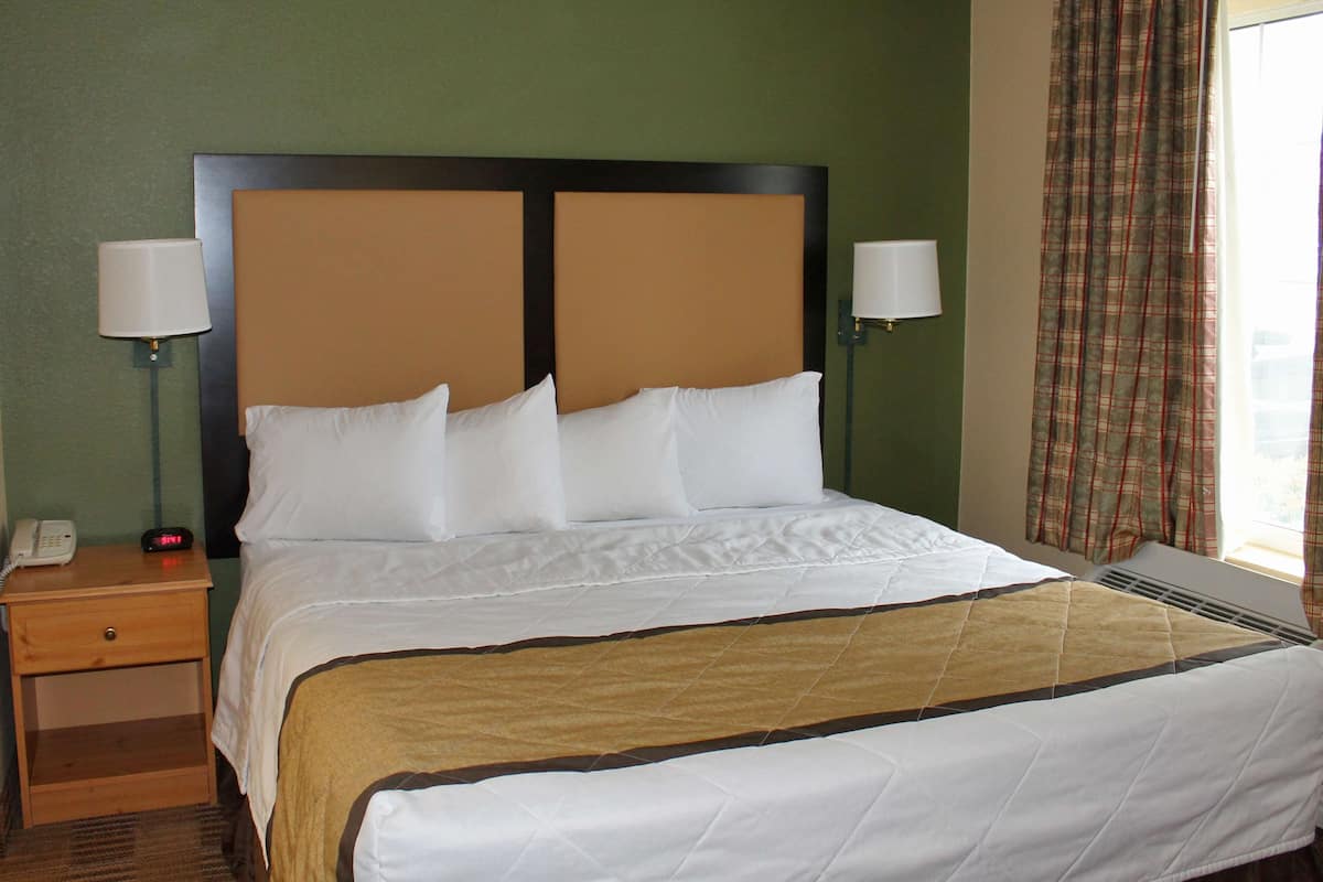 A hotel room with a large bed, two bedside lamps, a nightstand with a phone, and a window with plaid curtains.