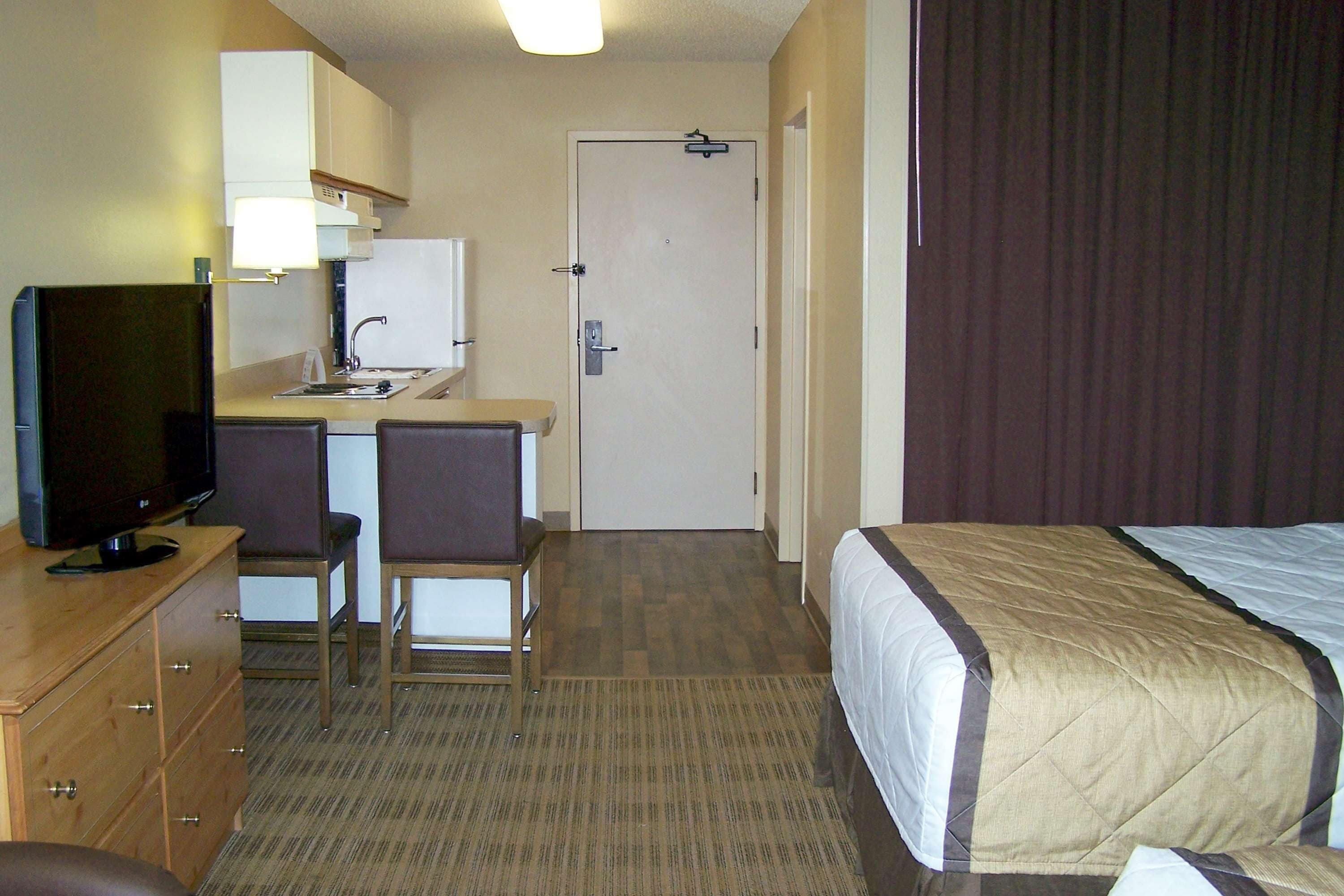 A hotel room with a bed, a desk with a chair, a television, and a door.
