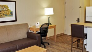 A hotel room with a brown leather sofa, a wooden desk with a lamp, a chair, and a small table. - Extended Stay America Suites Kansas City Overland Pk Nall Av (Overland Park)