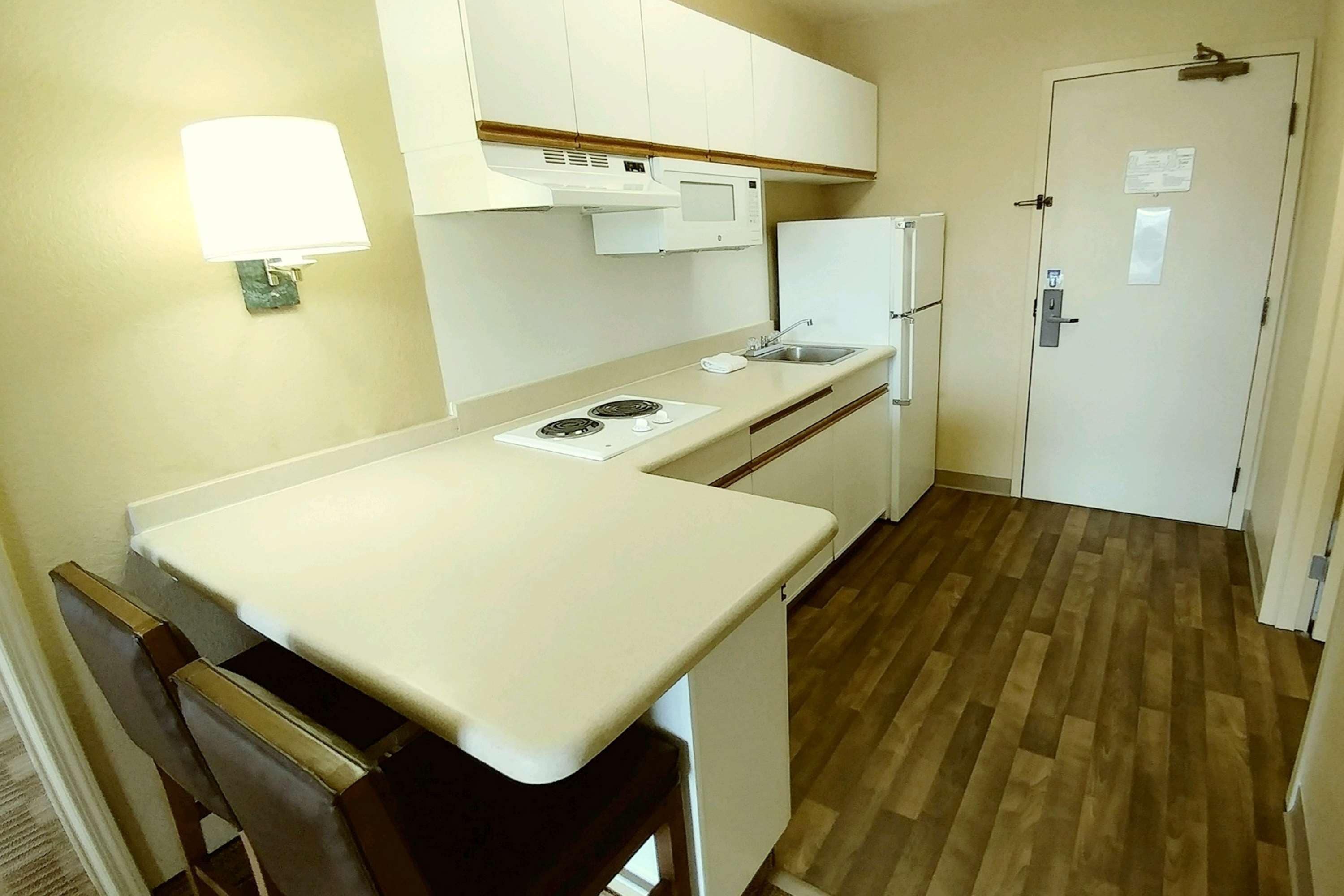 Une cuisine de taille réduite, dotée d’un plan de travail blanc, d’un four à micro-ondes, d’un réfrigérateur et d’un évier.