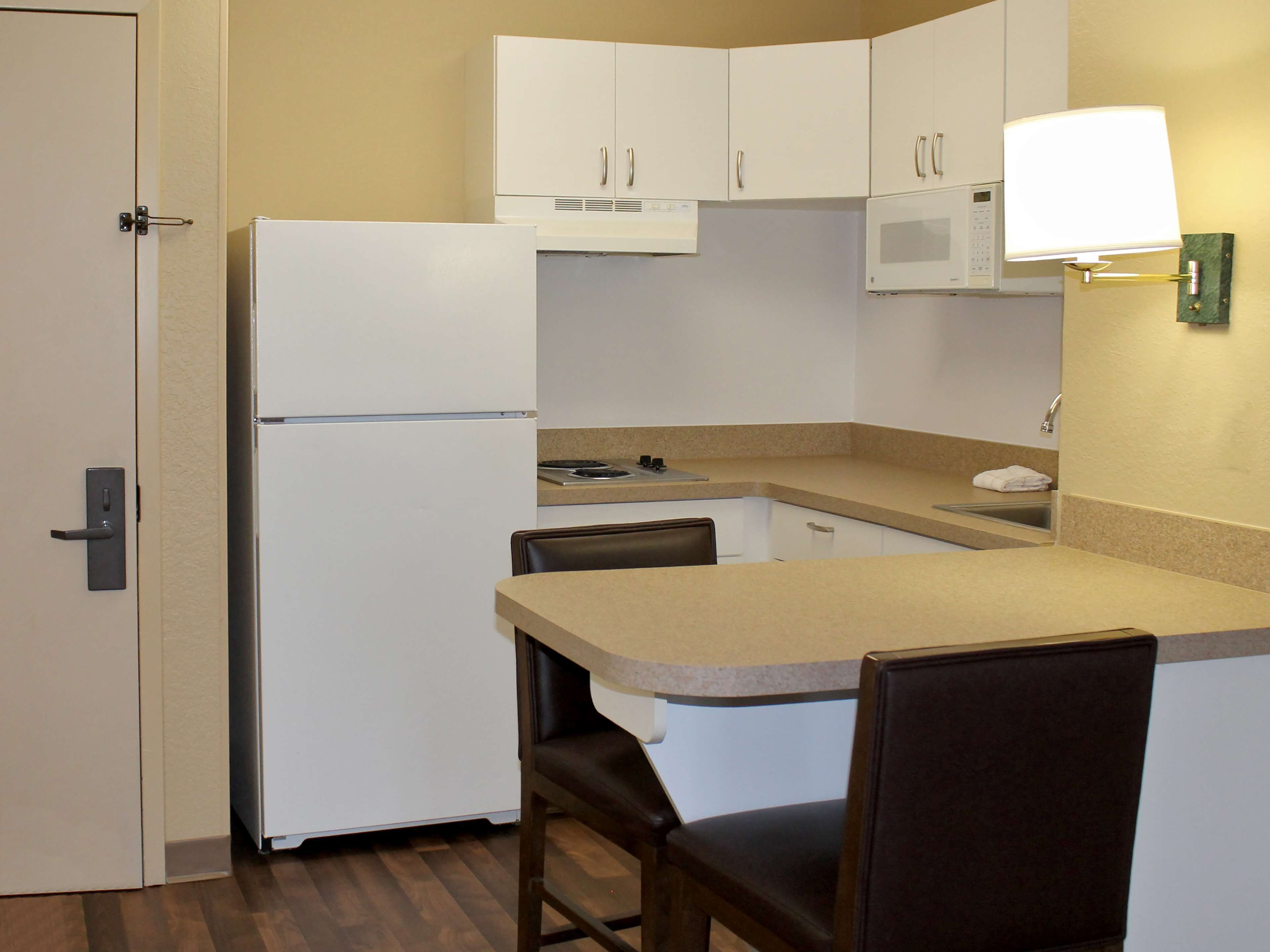Una cocina compacta con refrigerador, microondas y un pequeño comedor con una silla.