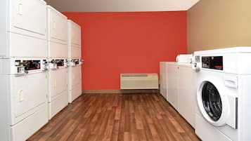 Un lavadero con varias lavadoras y secadoras, suelo de madera y una pared roja.