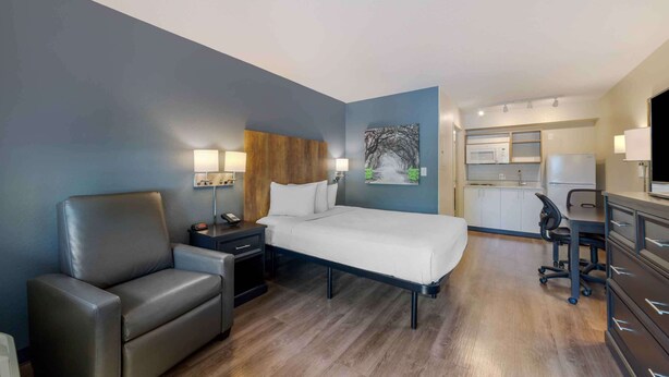 Een hotelkamer met een bed, een bureau, een stoel, een nachtkastje, een lamp en een schilderij aan de muur.