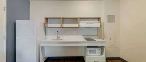 A compact kitchen with a white countertop, a built-in microwave, and a refrigerator.