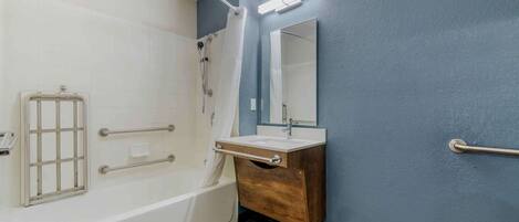 Un baño con bañera, tocador de madera, espejo y ducha con cortina.