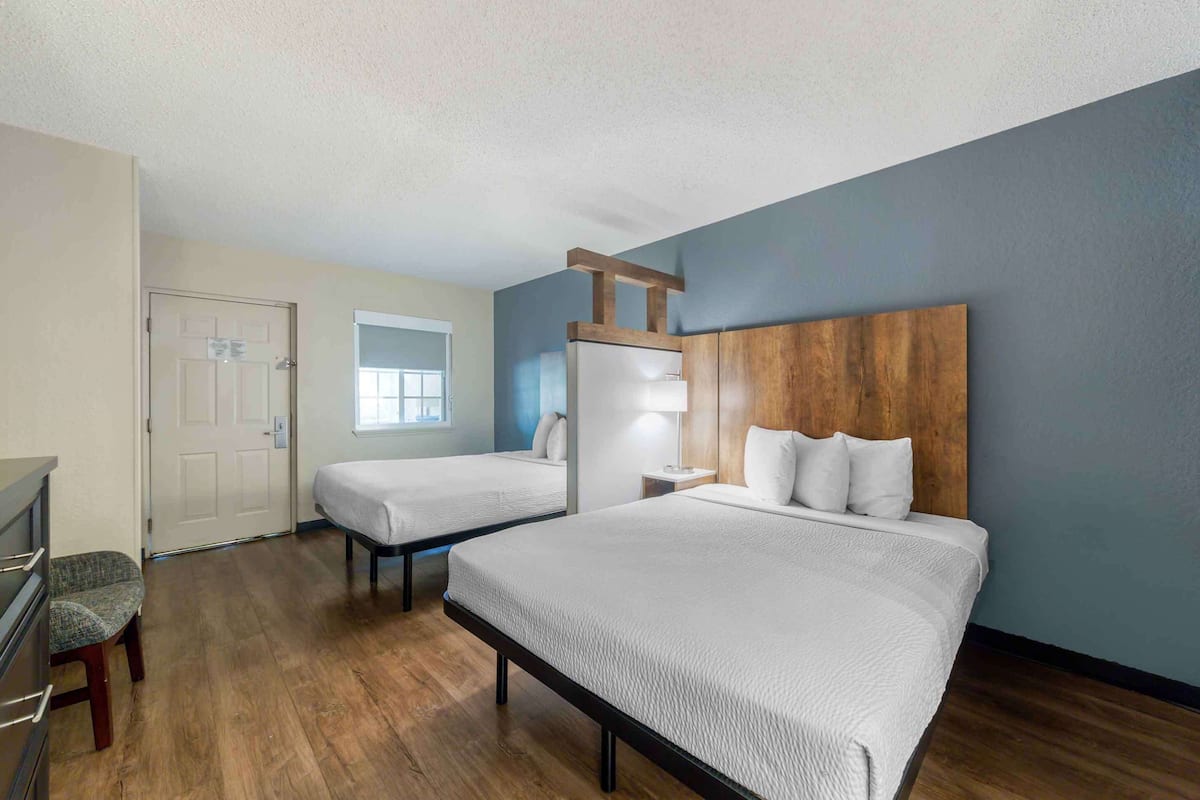 Una habitación de hotel con dos camas, un cabecero de madera, un escritorio con una silla y una ventana.