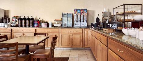 A kitchen with wooden cabinets, a granite countertop, a coffee station, and a buffet area.
