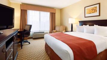A hotel room with a bed, a desk with a TV, a chair, a lamp, and a window with curtains.
