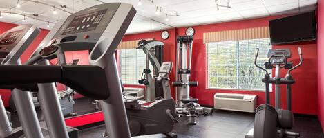 A gym with treadmills, weight machines, and a TV screen.