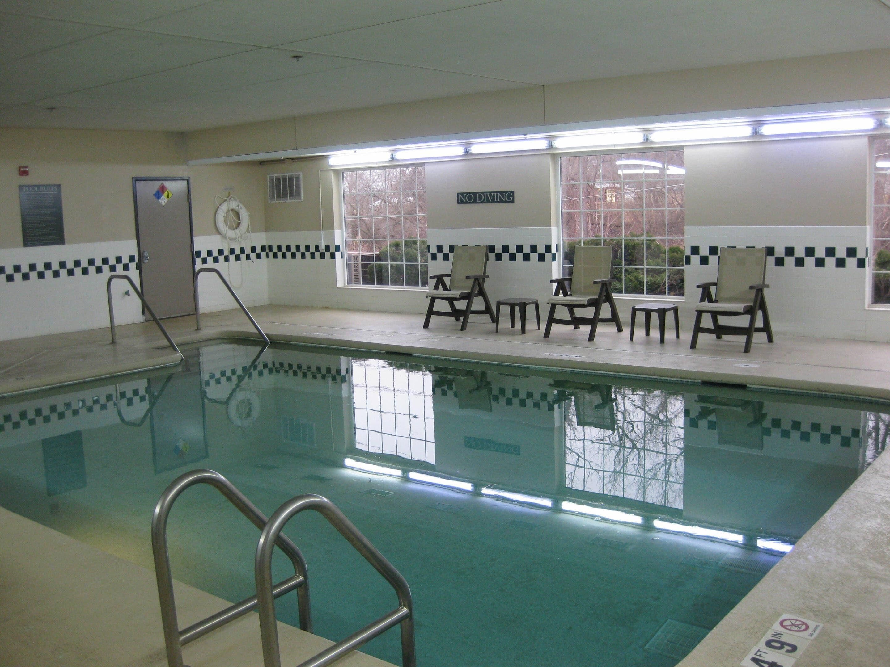 A swimming pool with a no diving sign, poolside chairs, and a lifebuoy.
