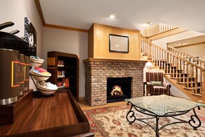 A living room with a fireplace, a staircase, a dining table, and a buffet area.