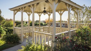 A gazebo with a ceiling fan, surrounded by well-maintained gardens and a clear view of the neighborhood.