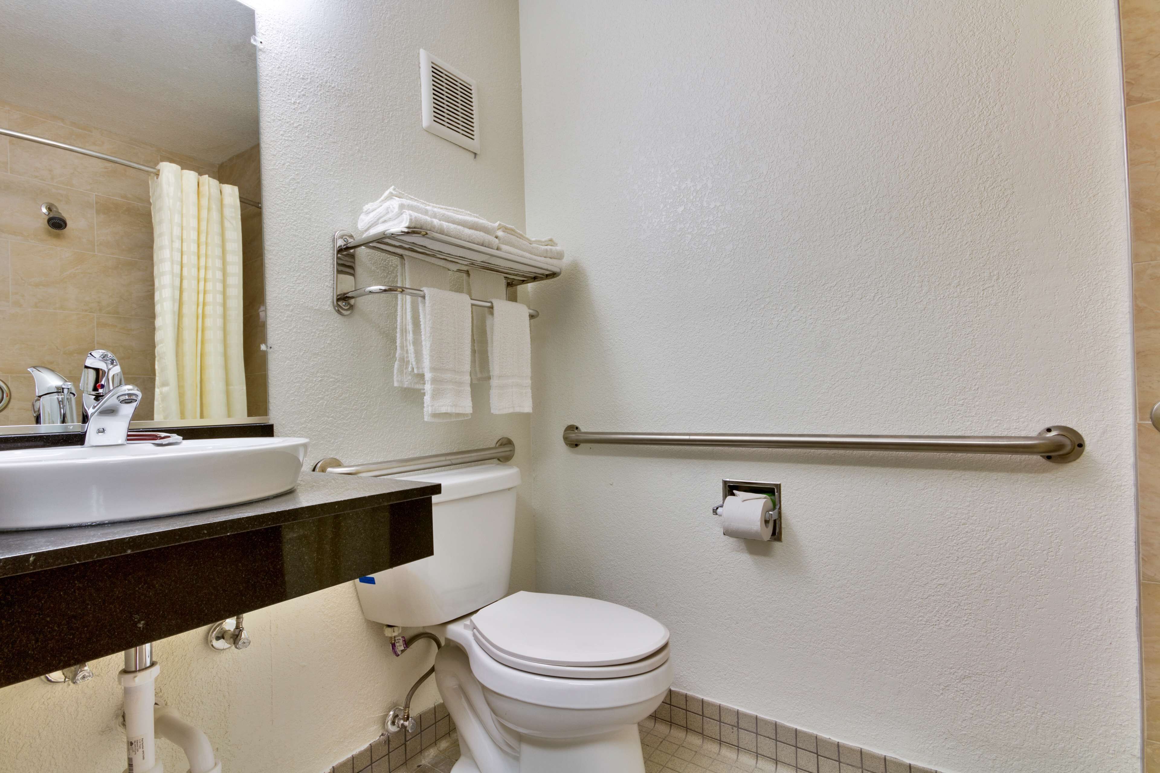 Un baño con lavamanos, inodoro y barras de apoyo.