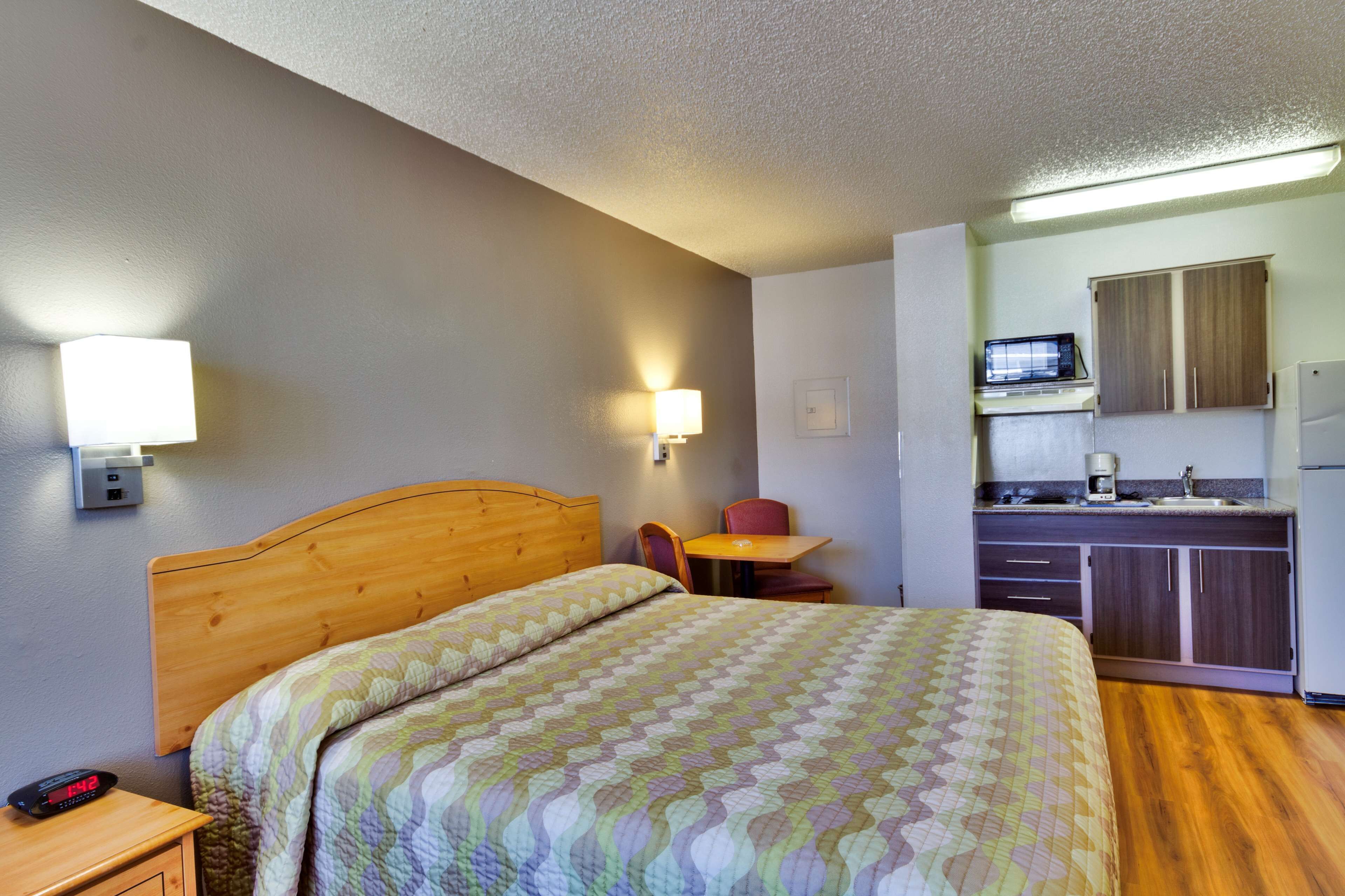 Ein Hotelzimmer mit einem hölzernen Bett, einer kleinen Küchenzeile und einem einzelnen Stuhl.