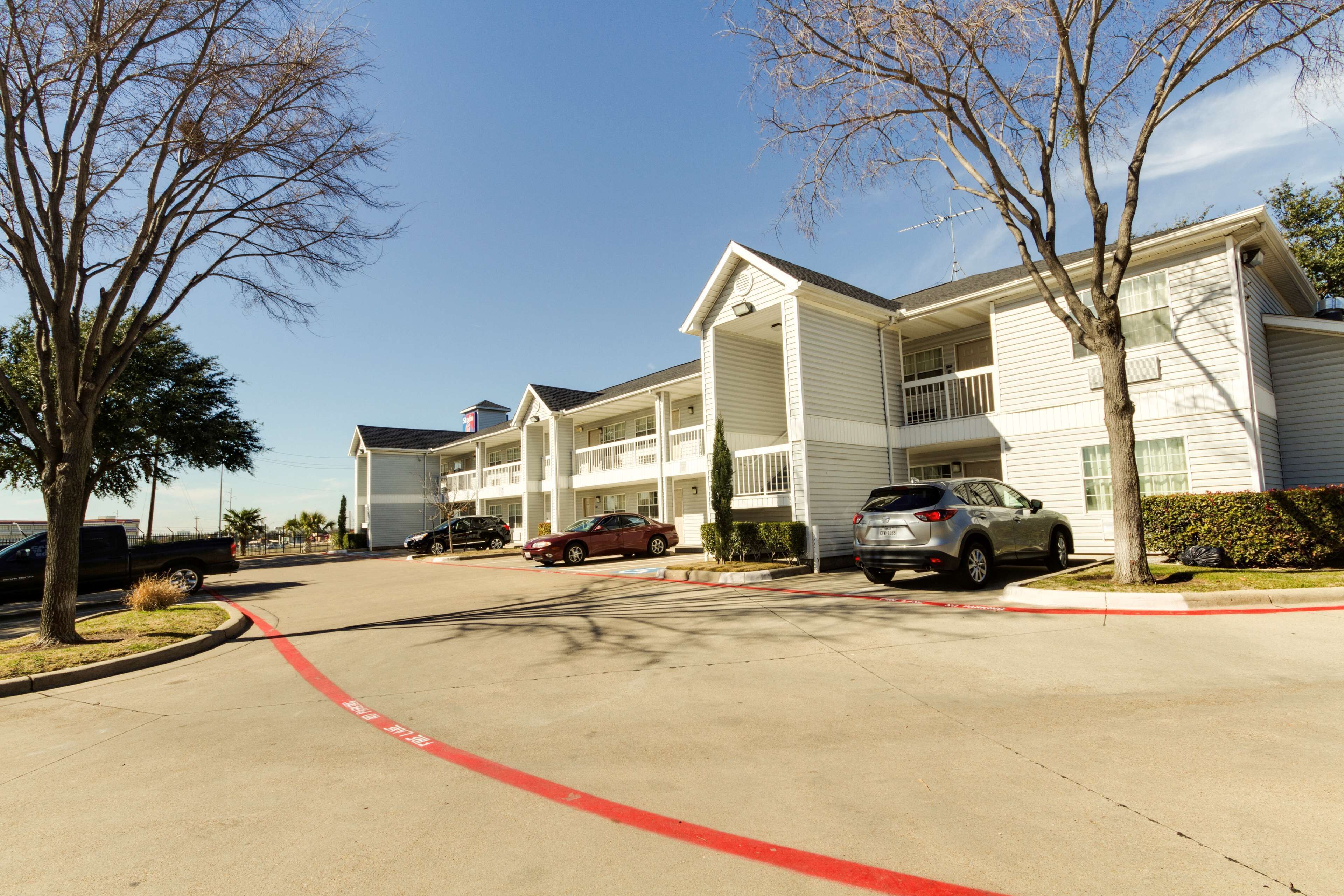 A multi-story hotel with a central courtyard, parking lot, and a clear sky.