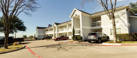A multi-story hotel with a central courtyard, parking lot, and a clear sky.