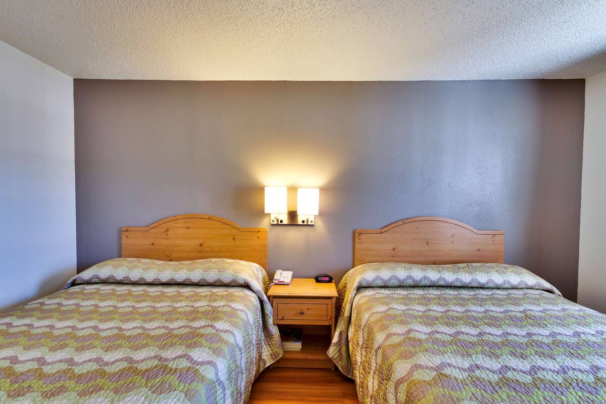 A double room with two beds, a wooden nightstand with a lamp, and a small drawer.