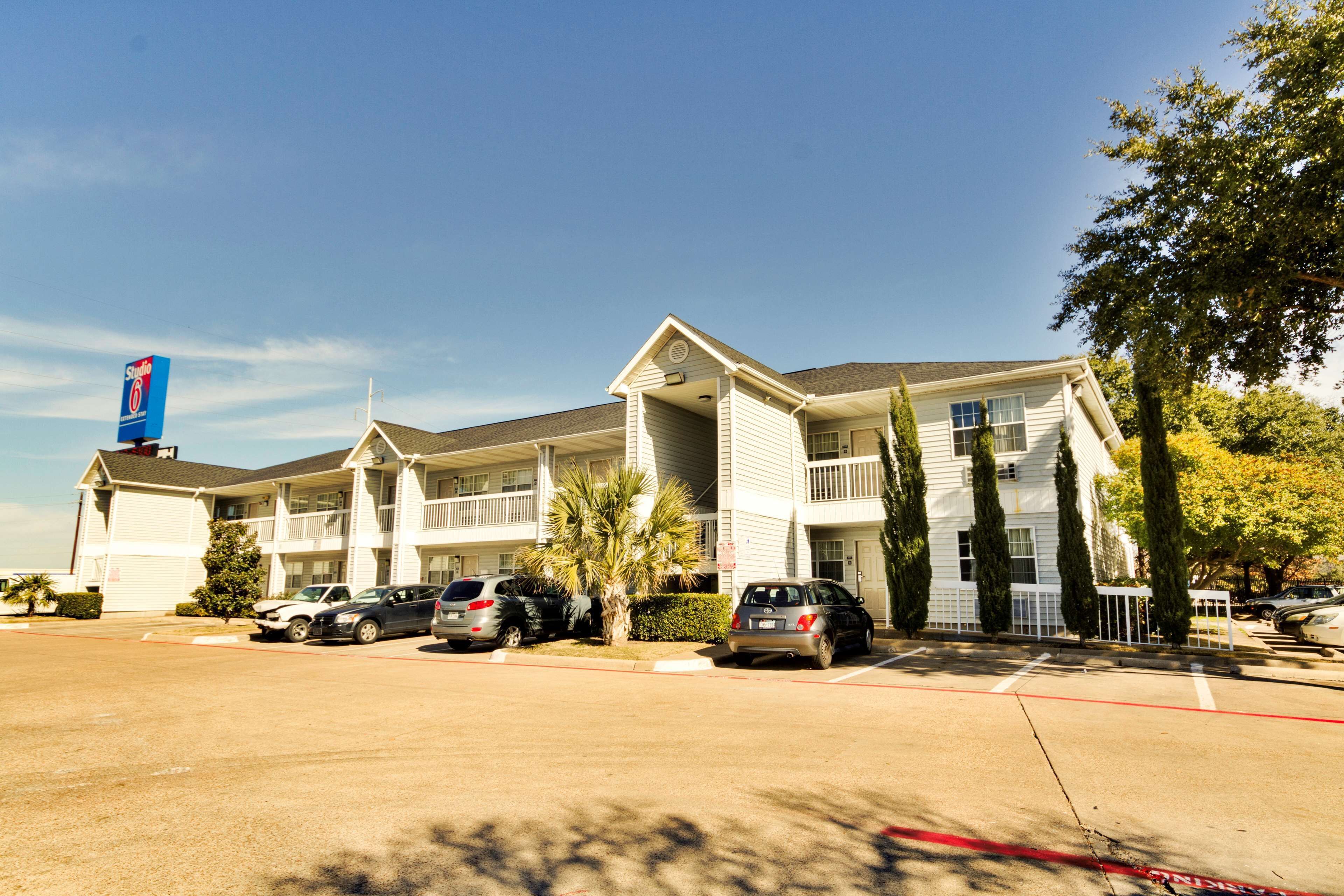 A motel with multiple-story buildings, a parking lot, and several cars parked in front.