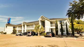 A motel with multiple-story buildings, a parking lot, and several cars parked in front.