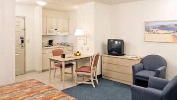 A hotel room with a bed, a desk with a chair, a television, and a small kitchenette.
