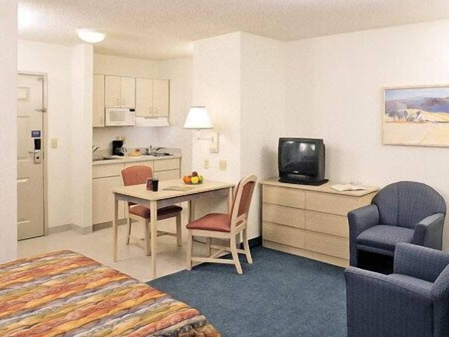A hotel room with a bed, a desk with a chair, a television, and a small kitchenette.