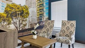 A room with a wooden table, two patterned chairs, a vase with flowers, and a cityscape mural on the wall. - Suburban Studios Raleigh - Crabtree Valley (Raleigh)