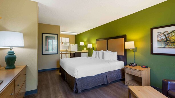 A hotel room with a bed, bedside tables, a desk, a chair, and a lamp. - Extended Stay America Suites Clearwater Carillon Park (Clearwater)