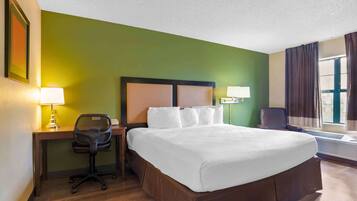 A hotel room with a large bed, a desk with a chair, two bedside lamps, and a window with curtains.