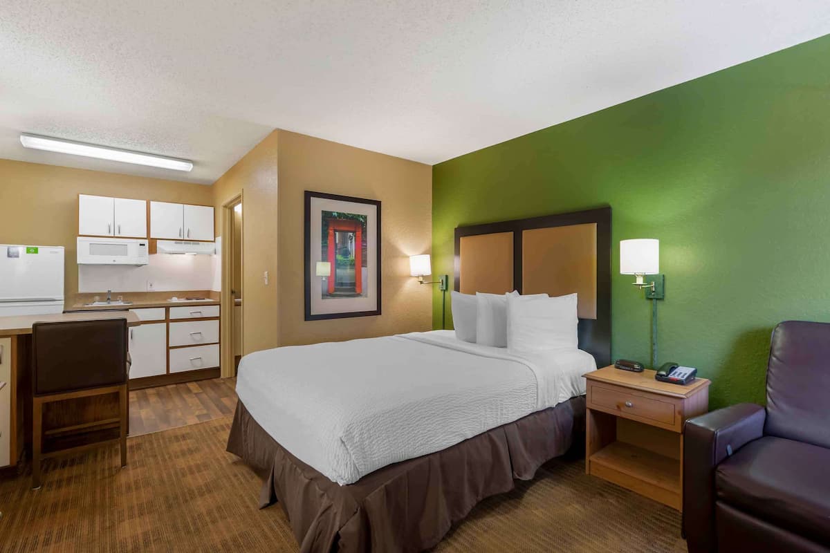 Ein Hotelzimmer mit Bett, Schreibtisch, Küchenzeile und einer Wand in Grüntönen.