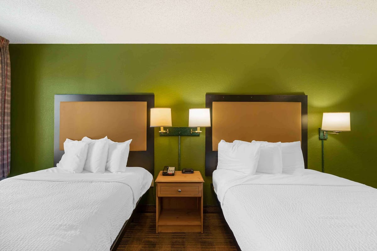 Ein Hotelzimmer mit zwei Betten, grünen Wänden und Nachttischlampen.