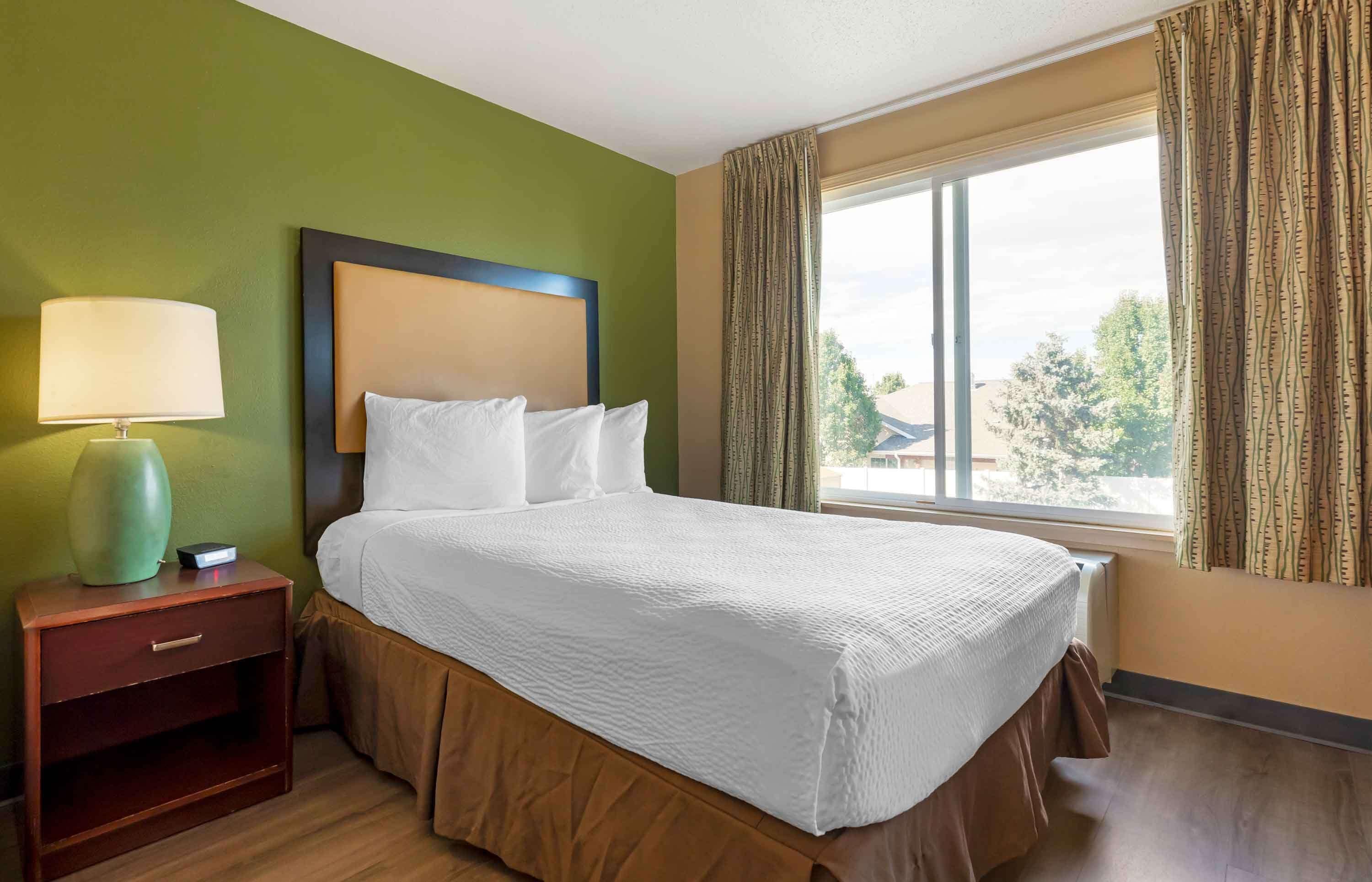 A hotel room with a bed, a nightstand, a lamp, and a window with curtains.
