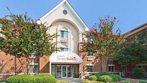 A hotel entrance with a sign reading "SONESTA Simply Suites," surrounded by well-maintained landscaping and trees.
