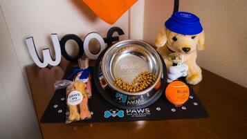 A table with a dog bowl, a toy, a treat bag, and a paw print placemat.