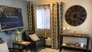 A cozy living room with a blackboard, patterned curtains, a large wall clock, and a wooden console table with candles.