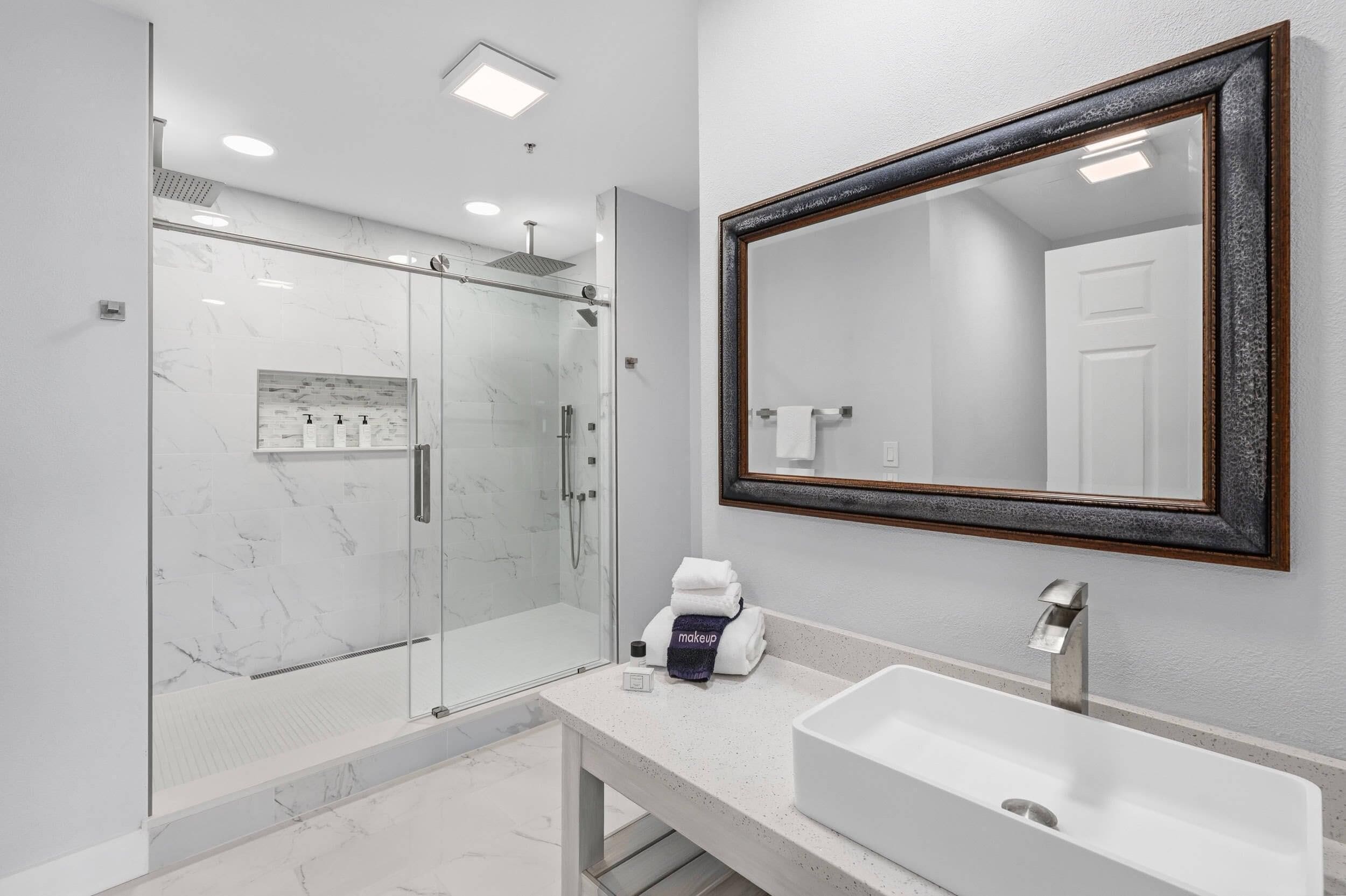 Une salle de bain moderne avec une douche à parois de verre, un grand miroir et un lavabo blanc.