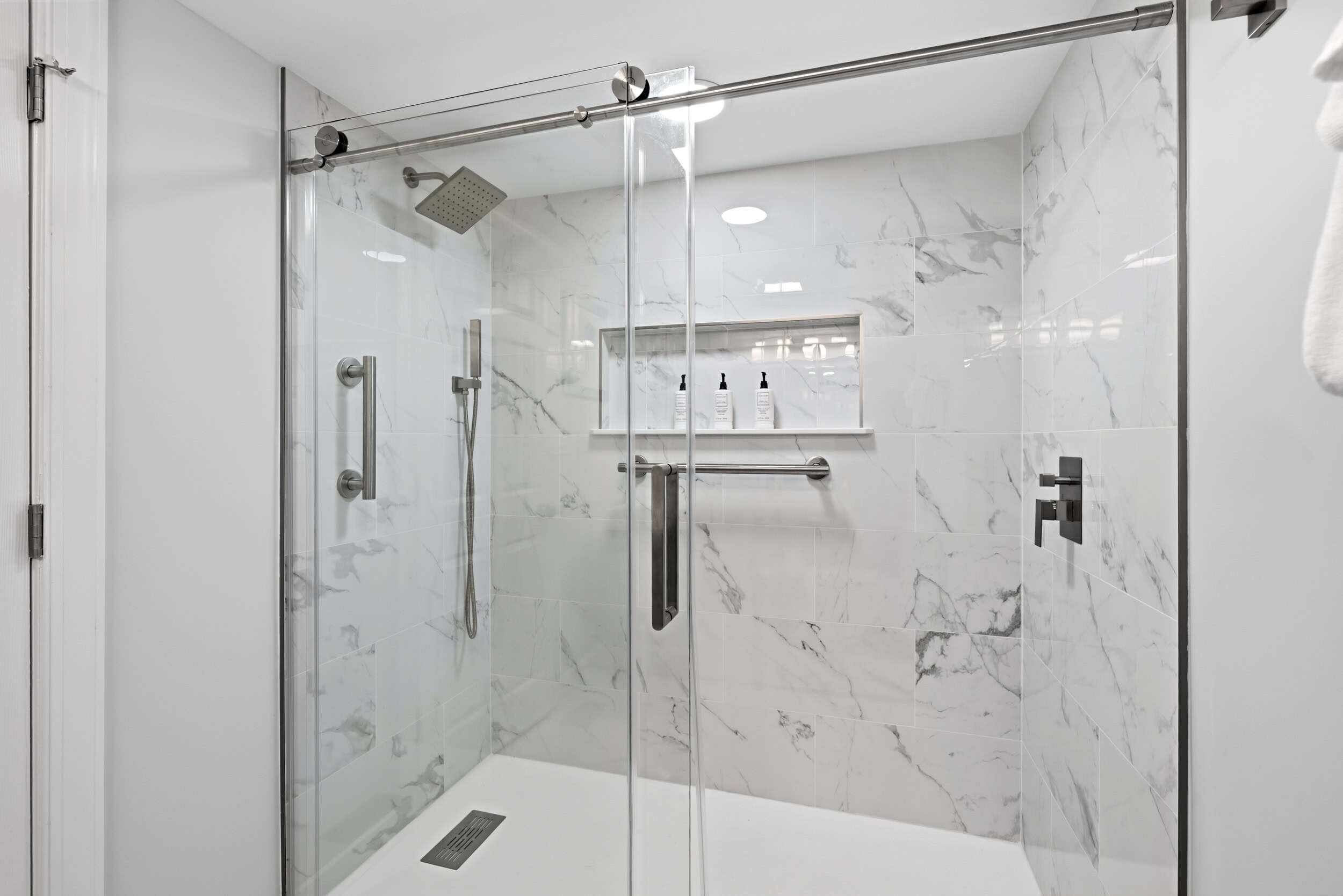 A modern bathroom with a glass-enclosed shower, marble tiles, and a built-in shelf with toiletries.