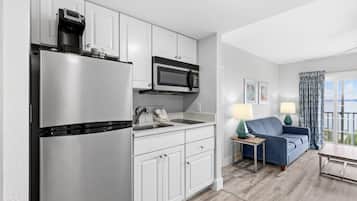 A modern kitchen with a refrigerator, microwave, and sink. There is a blue sofa and a table with lamps in the living area.