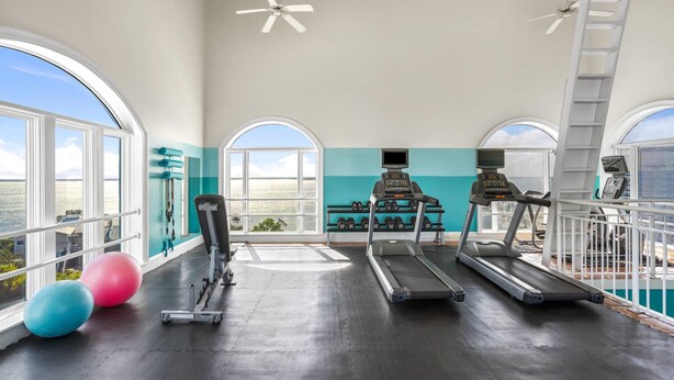 Un gimnasio con cintas de correr, mancuernas y pelotas de ejercicio, con amplias ventanas y vistas al océano.