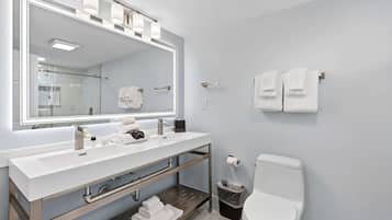 Ein modernes Badezimmer mit großem Spiegel, zwei Waschbecken, Toilette und Mülleimer.