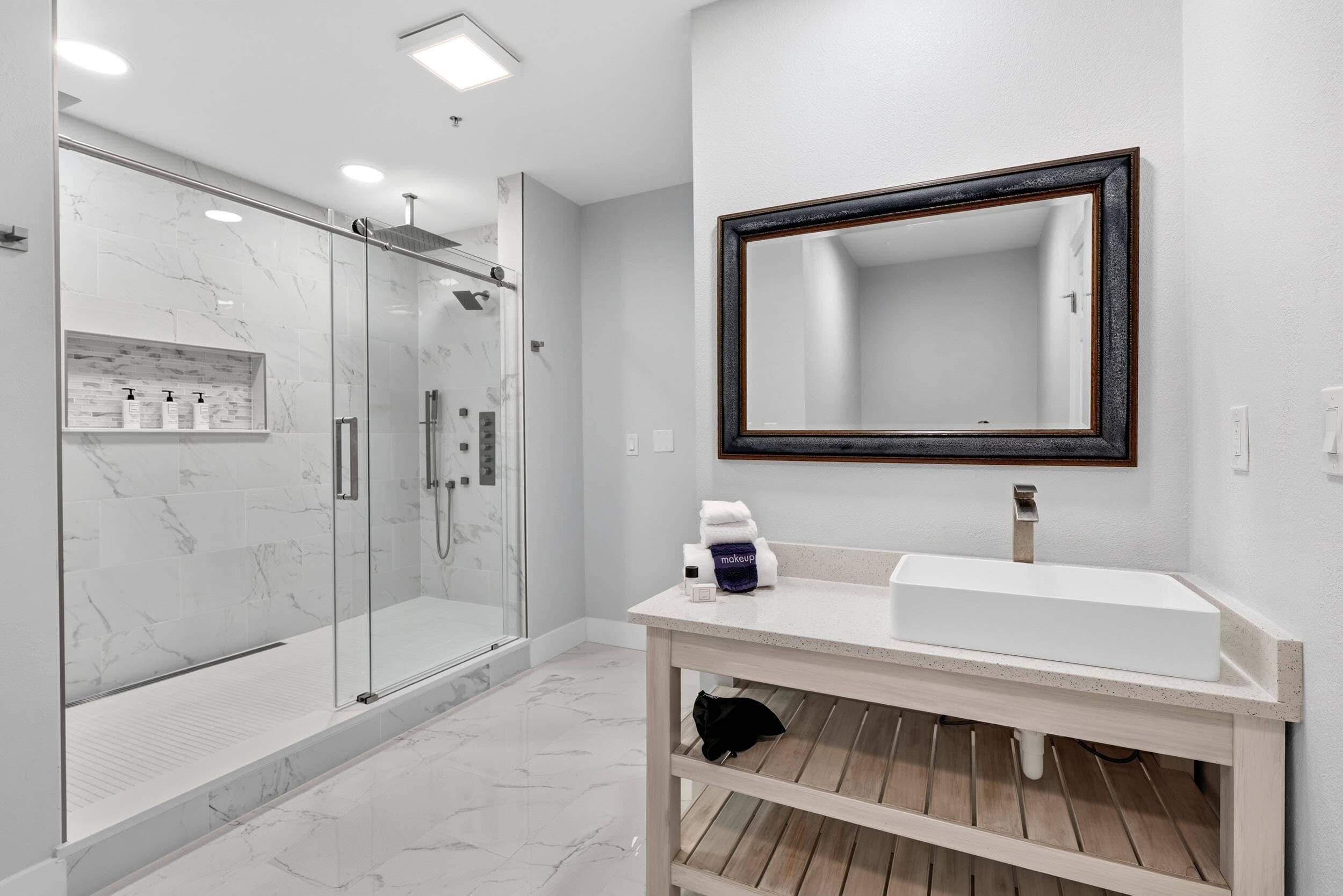 Un baño moderno con cabina de ducha de vidrio, un lavabo blanco y un espejo grande con marco oscuro.
