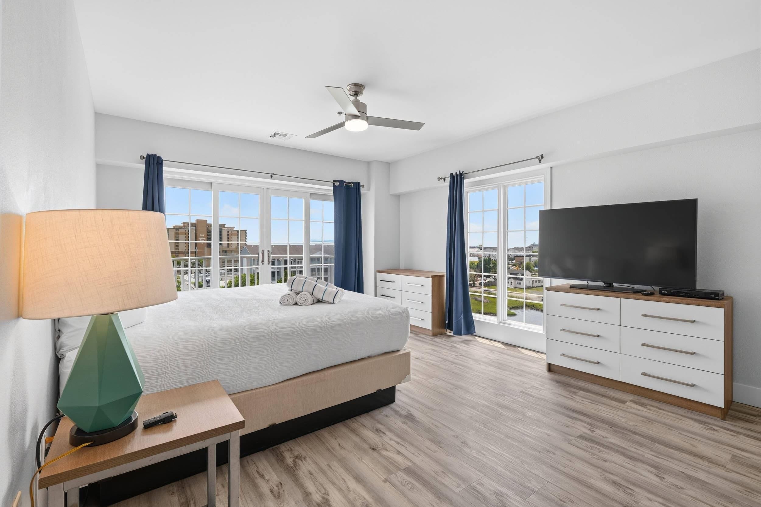 A modern hotel room with a bed, a TV, a desk, and a view of the city.