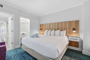 Une chambre d’hôtel avec un grand lit, une tête de lit en bois, deux tables de chevet avec des lampes, une armoire blanche et un tapis à motifs.