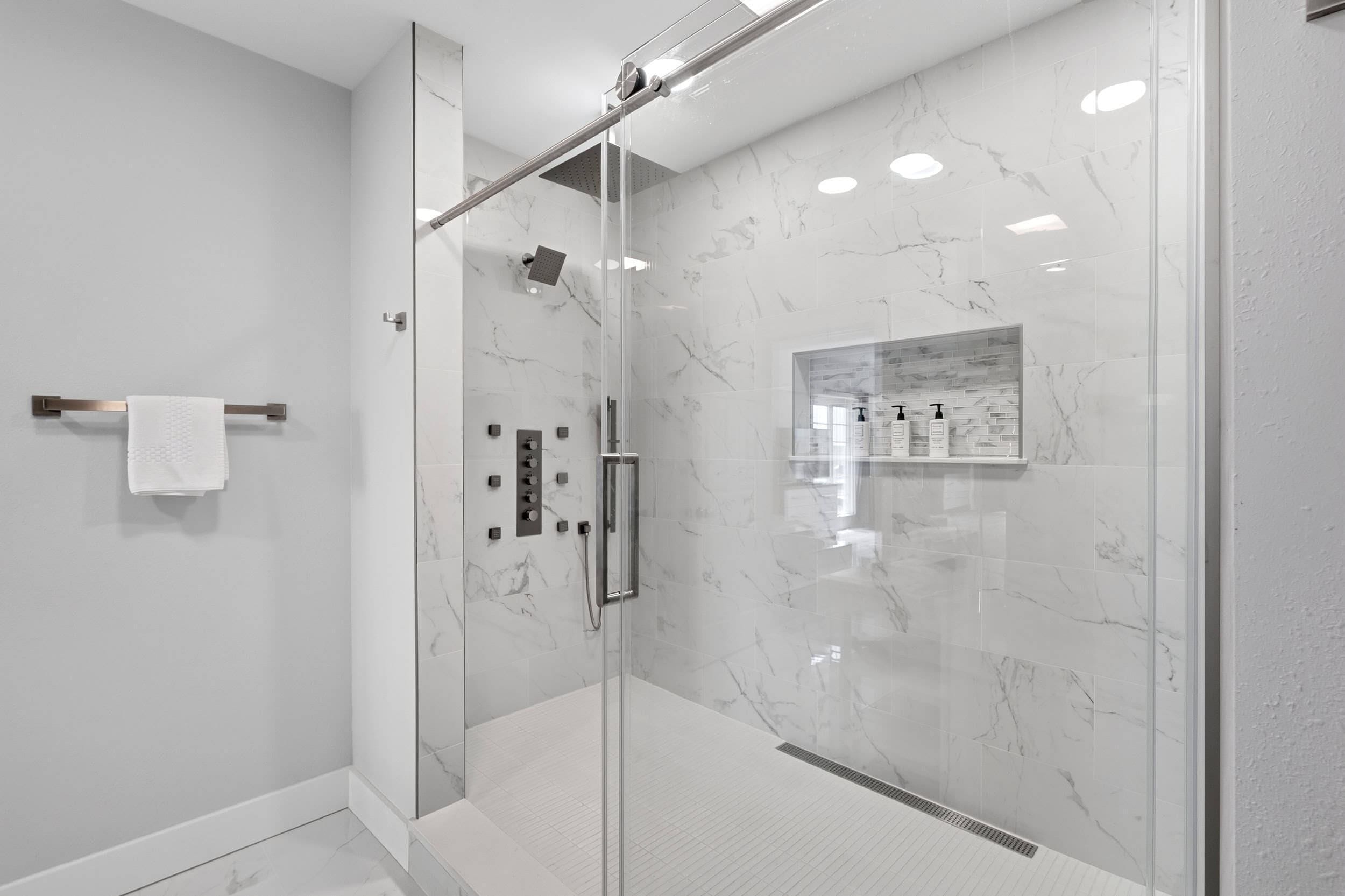 A modern bathroom with a glass-enclosed shower, marble walls, and a white towel on a metal rack.